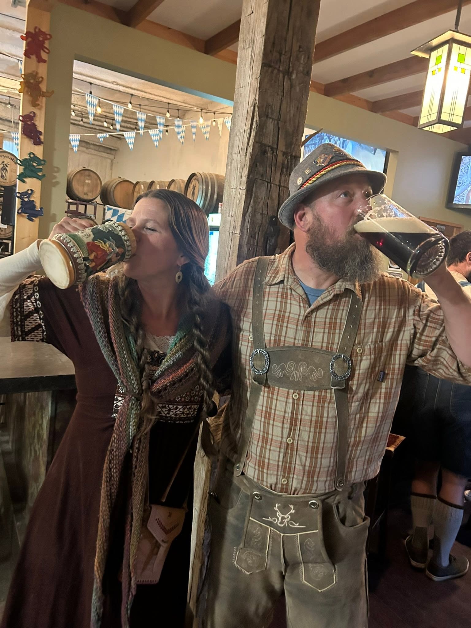Two regulars in Bavarian dress raising steins in the taproom, barrels behind them